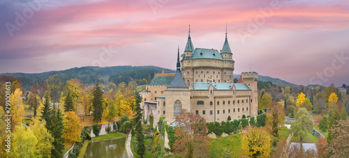 Bojnice Castle. Panoramic, Aerial view of neo-gothic romantic, fairytale castle in colorful autumn landscape under pink colored sunset sky.  Slovakia.