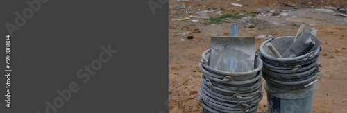 Banner Image of Powder Cement and sand mixing bucket tank, trowel, and plastering equipment in construction site.