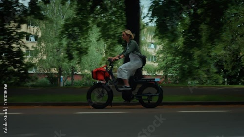 Handheld real life looped shot of woman ride cute electric city bike downhill on fast speed on busy street. cars pass by she rides on bike lane. Commuting and cycling in everyday life
