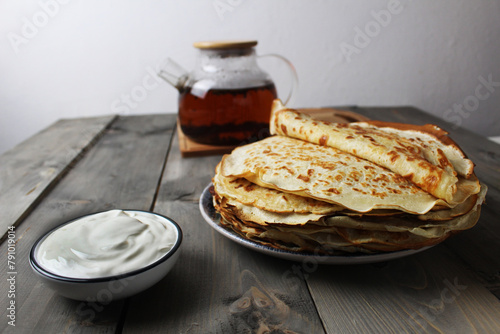 The crepe pancake is stacked on a plate with sour cream and a cup of tea. Russian Breakfast