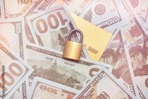 A gold lock and a gold bank card on the background of hundred-dollar bills. Protection of money, safe storage, financial security. Protection of gold credit card data.