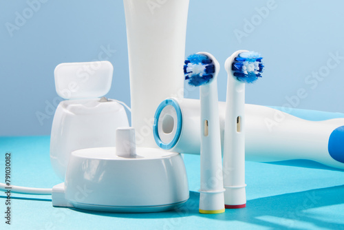 Electric toothbrush with contactless charging and oral hygiene products on pastel background.Oral hygiene supplies on a blue color background.