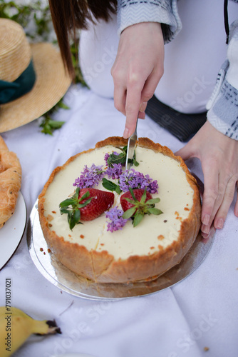 Woman cuts a cake on summer picnic with strawberry and lilac