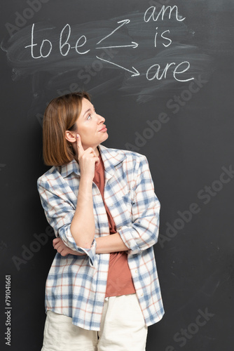 In the English classroom, a focused female student stands confidently before the blackboard, actively participating in a lesson about the verb "To Be"
