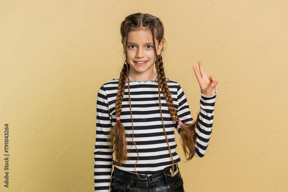 Happy young preteen child girl kid showing victory sign hoping for success and win doing peace gesture smiling with kind optimistic expression celebrate. Teenager children isolated on beige background Happy young preteen child girl kid showing victory sign hoping for success and win doing peace gesture smiling with kind optimistic expression celebrate. Teenager children isolated on beige background