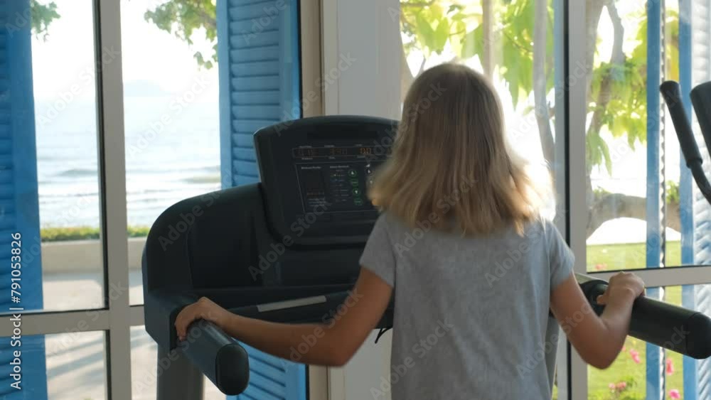 Rear view of cute child girl jogging on a treadmill during sports ...
