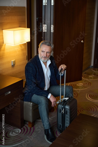 Concentrated businessman with suitcase sitting on leather chair and looking away