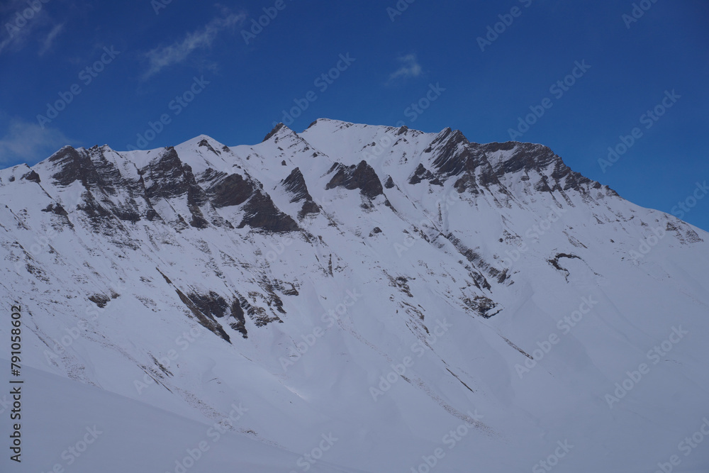 The snow-covered peaks of the mountain range under a blue sky and white clouds, Devil's Valley in the Caucasus mountains, Gudauri, Georgian Military Highway, Georgia