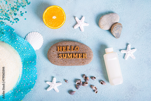 Hello summer text on stone, hat, suntan lotion, orange, starfish and seashells on blue background top view