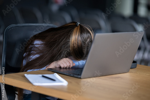 A schoolgirl girl fell asleep during an online lesson. She rested her head on the laptop.