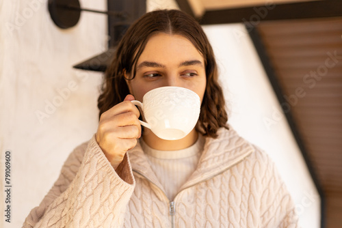 girl in a sweater drinks a cup of coffee