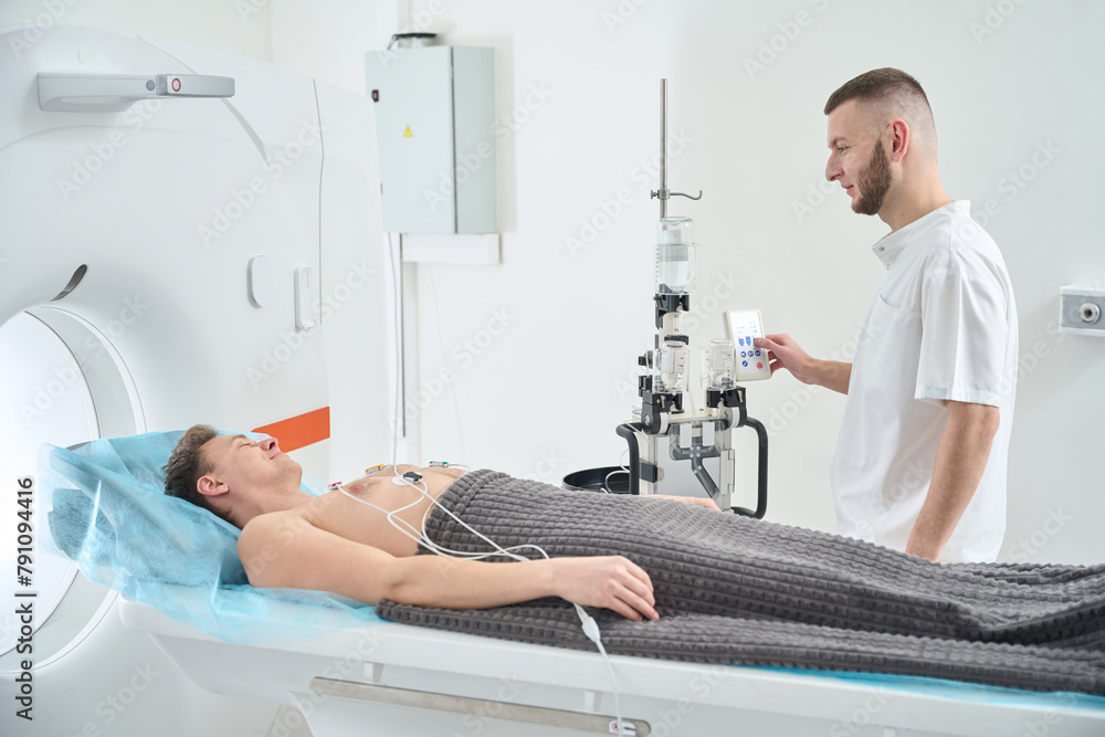 Obraz premium Doctor preparing man for contrast-enhanced ECG-gated coronary CT angiography