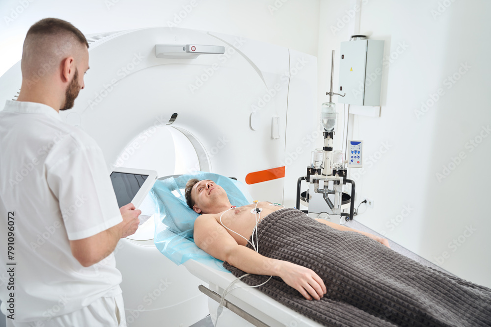 Radiographer monitoring adult person before ECG-gated coronary CT angiography Radiographer monitoring adult person before ECG-gated coronary CT angiography