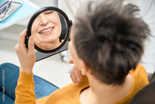 Woman client checking her smile and state of teeth after hygienic cleaning