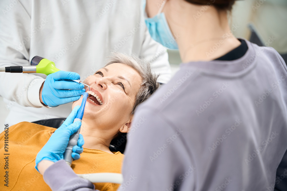 Woman smiling while dentist keeping out procedure of airflow teeth cleaning Woman smiling while dentist keeping out procedure of airflow teeth cleaning