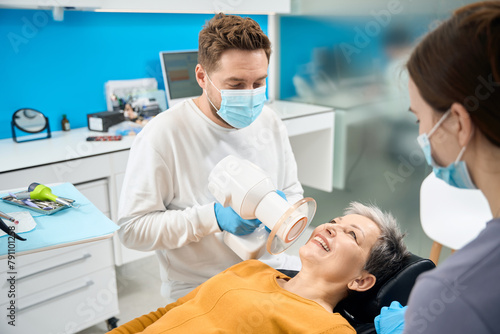 Aesthetic dentist in face mask holding portable dental x-ray near patient