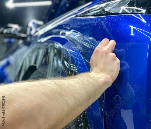 A car wrapping specialist applies a polyurethane film to the car close-up. Selective focus. PPF protective film against chips and scratches. Car wrapping. 