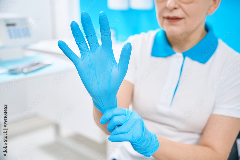 Woman dental hygienist putting on protective medical gloves