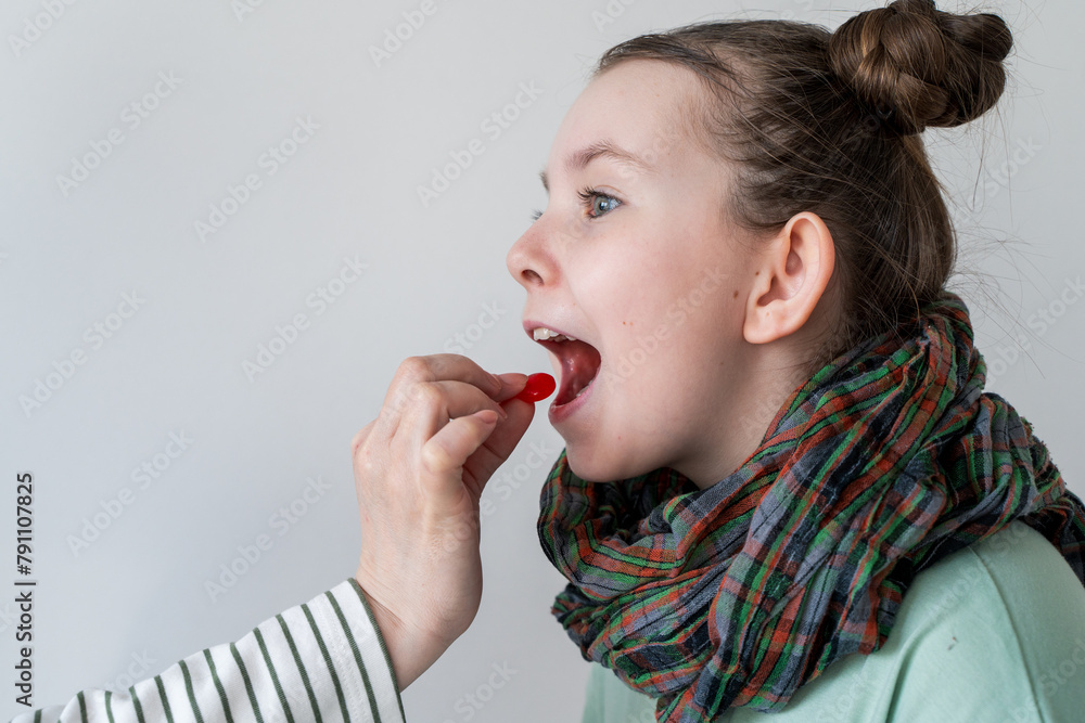 A little girl with a sore throat takes a pill. Mom's hand gives the pill to the girl. A little girl with a sore throat takes a pill. Mom's hand gives the pill to the girl.