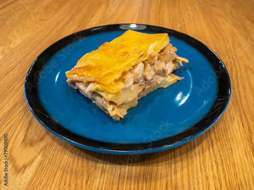 A piece of Potato casserole with mushrooms and chicken covered by cheese crust on the dark blue plate