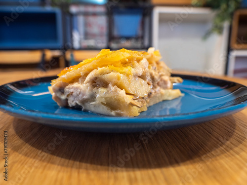 A piece of Potato casserole with mushrooms and chicken covered by cheese crust on the dark blue plate