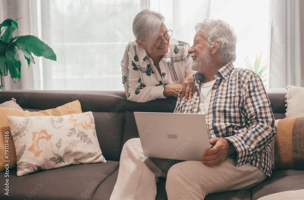 Relaxed senior white haired couple sitting on home sofa using computer have fun together enjoying happy retirement lifestyle in good mood Relaxed senior white haired couple sitting on home sofa using computer have fun together enjoying happy retirement lifestyle in good mood
