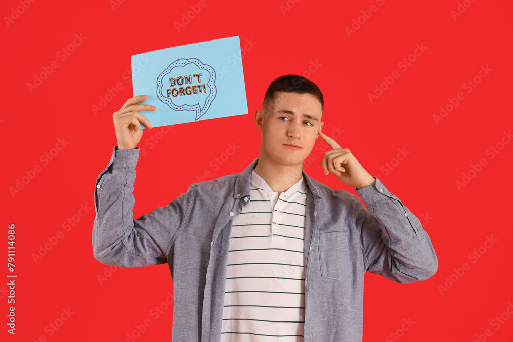 Thoughtful young man holding paper with text DON'T FORGET on red background Thoughtful young man holding paper with text DON'T FORGET on red background