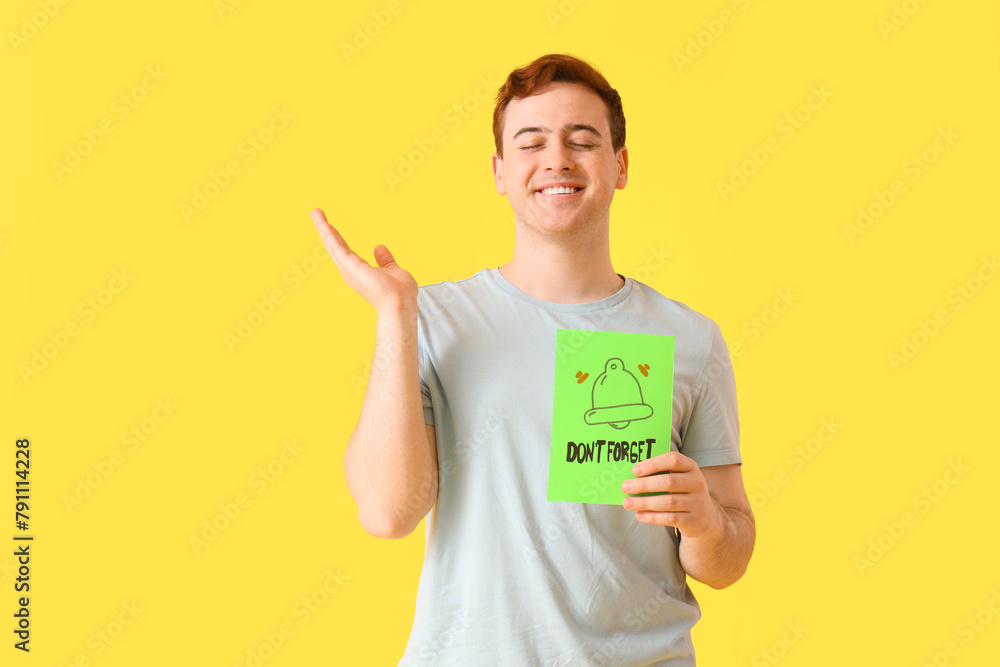 Young man holding paper with text DON'T FORGET and drawn bell on yellow background Young man holding paper with text DON'T FORGET and drawn bell on yellow background
