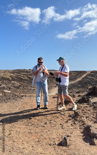 Outdoor activity in nature concept. Senior father and middle aged son have fun hiking together along the sea enjoying healthy lifestyle and freedom. Blue sky
