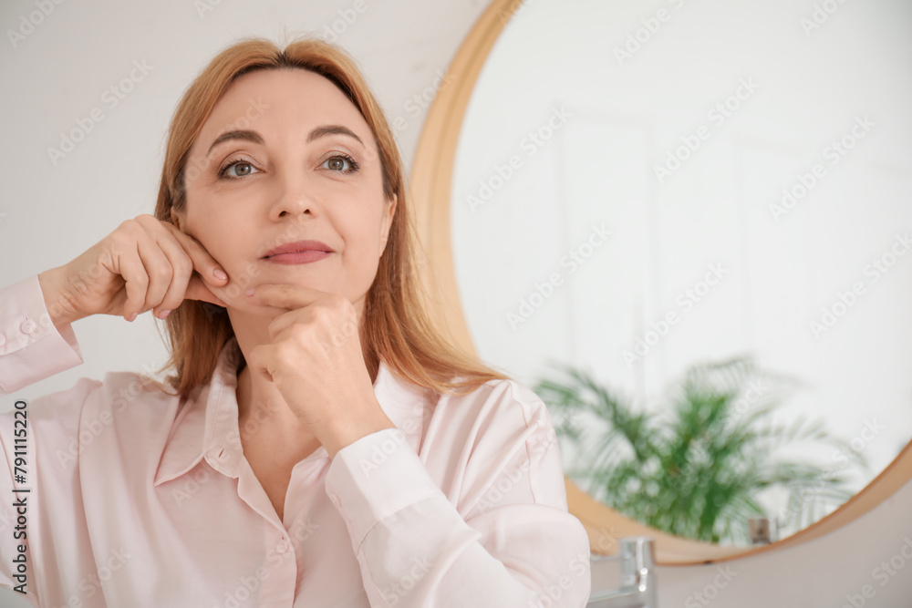 Beautiful mature woman doing face building exercise in bathroom Beautiful mature woman doing face building exercise in bathroom