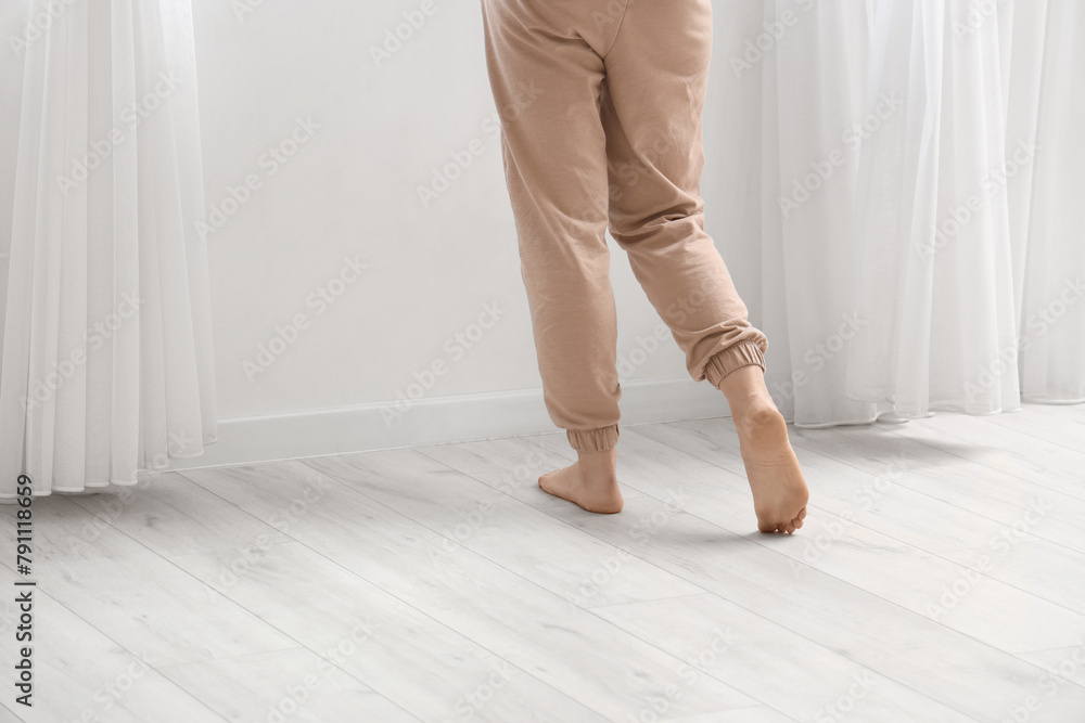 Barefoot woman walking on laminate floor in room, back view Barefoot woman walking on laminate floor in room, back view