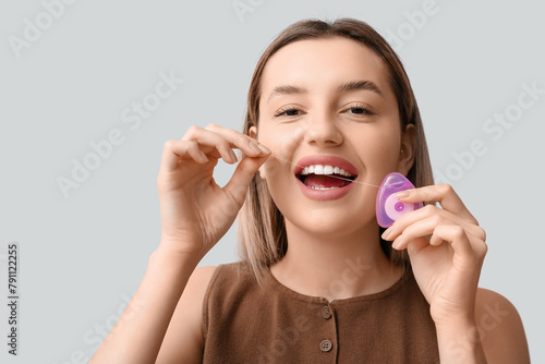 Young woman cleaning teeth with floss on light background, closeup