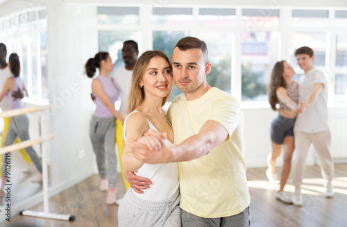 Happy caucasian man and girl in sportswear dancing cha-cha-cha dance in modern dance studio during group class