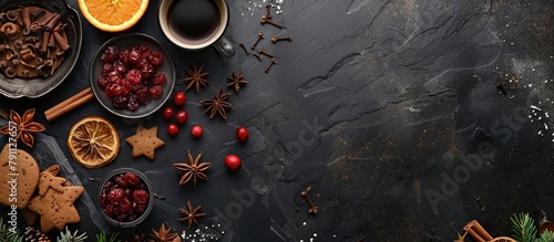 Christmas baking ingredients including gingerbread  fruitcake  and seasonal beverages on a black stone surface with cranberries  dried oranges  cinnamon  and spices. Top view with space for text.
