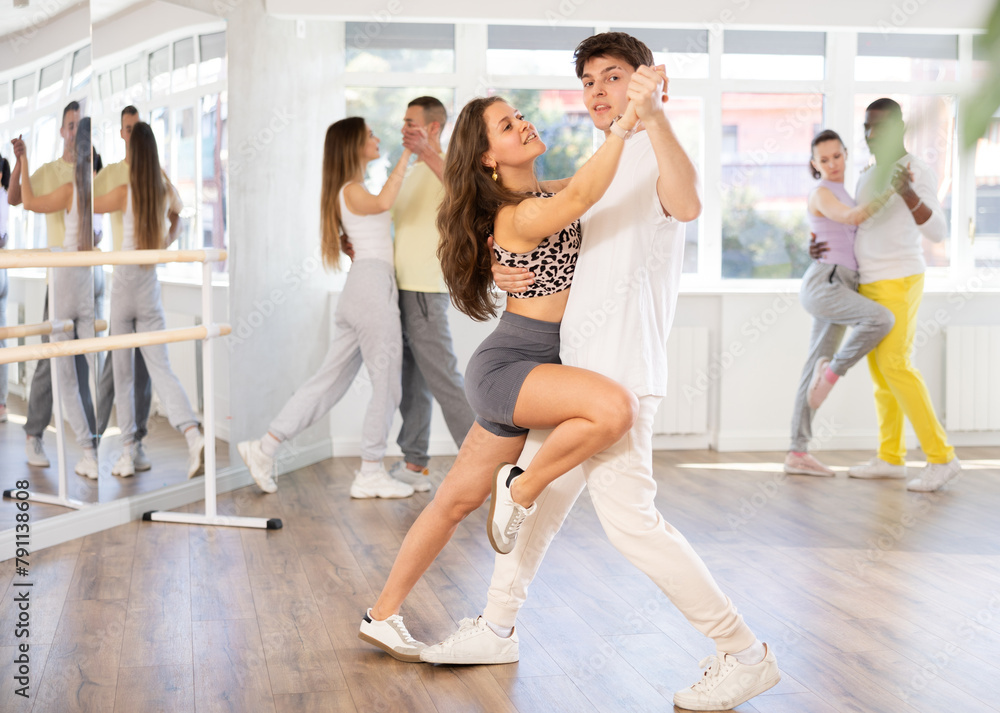 Girl paired with young man practices movements of Latin tango dance and trains to perform movements during lesson in choreography studio.