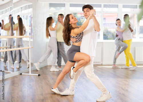 Girl paired with young man practices movements of Latin tango dance and trains to perform movements during lesson in choreography studio.