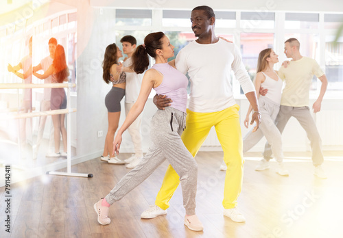Happy African american man in pair with young woman dancing and training latin dance movements in modern ballroom together