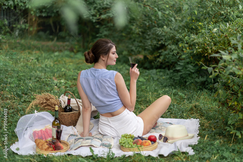 Smiling beautiful young girl with dark long hair in summer on picnic in nature, near fruits, wine, croissants