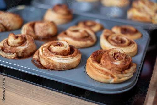 Cinnamon rolls with a rich, brown color, resting in a nonstick baking pan, focus on the spiraling dough, a blurred background, homemade snack.