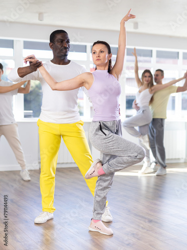 Positive african american man and female partner dancing with multiethnic active people enjoying social dance during group class in modern sport studio