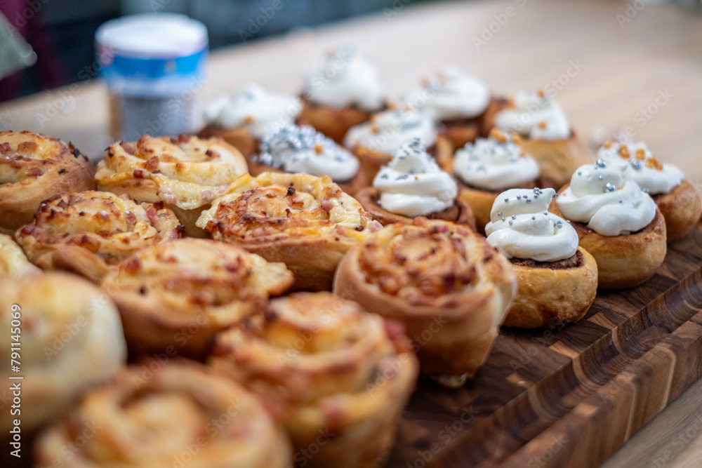 A selection of cinnamon rolls, some iced with silver dragees, on a wooden surface, blurred background hinting at a casual setting.
