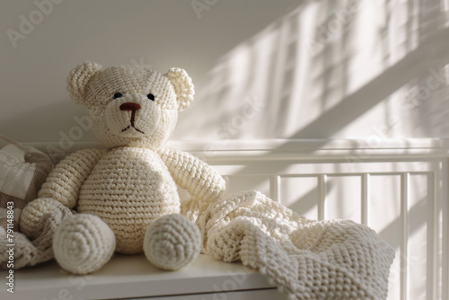 Handmade crochet teddy bear doll sitting on white drawer commode in baby room. Kid room interior, white walls with shadows and wooden furniture photo