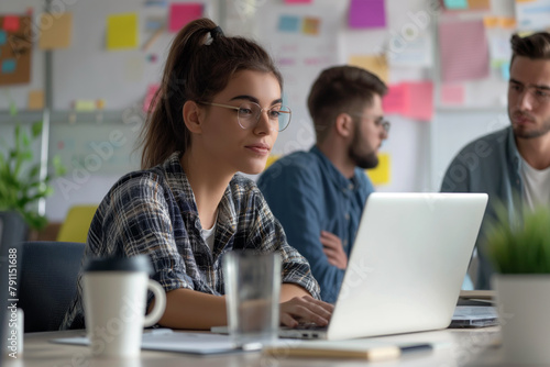 Focused team collaboration in modern office. Female business woman and man team working on laptop in office, while sitting at desk with whiteboard behind her.