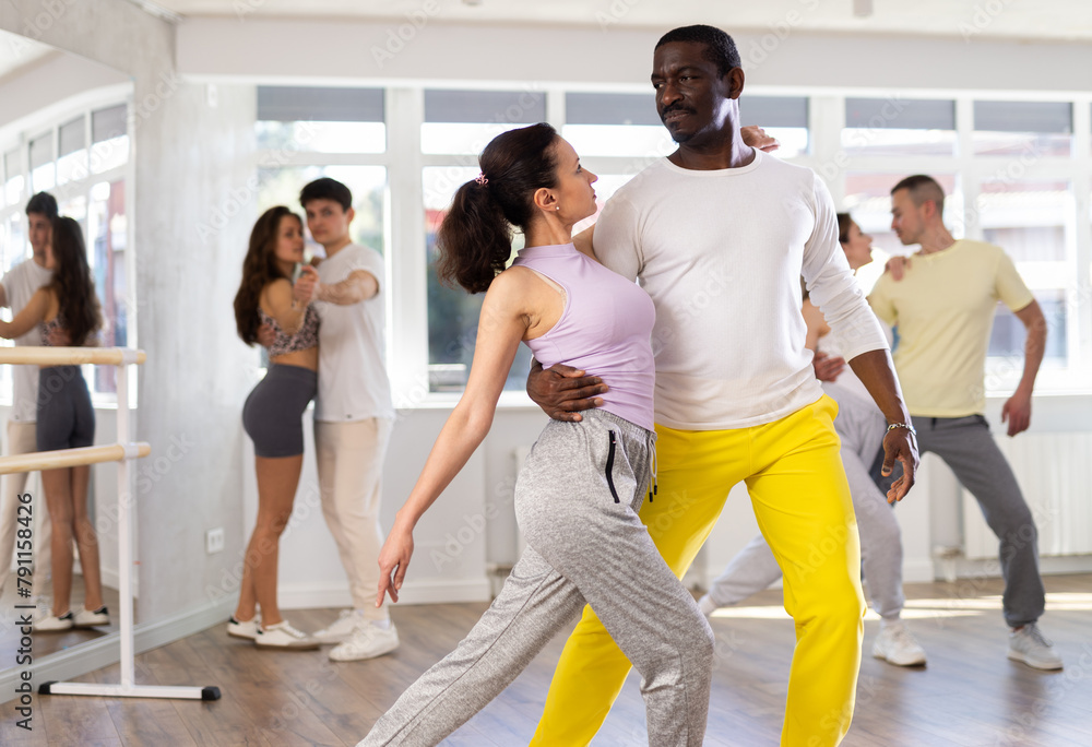 Positive young adult woman learning to dance tango with male partner in choreography class, performing elegant support