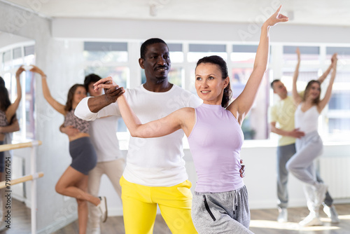 Positive african american man and female partner dancing with multiethnic active people enjoying social dance during group class in modern sport studio