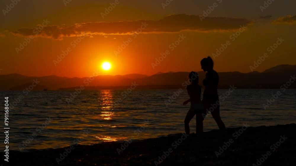 Travelers nightfall stroll by ocean waves. A view of woman with teen strolling along the bay against dusk horizon in summer. A concept of summer family resort. Travelers nightfall stroll by ocean waves. A view of woman with teen strolling along the bay against dusk horizon in summer. A concept of summer family resort.