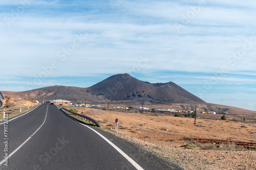 Driving car on black asphalt road through white sandy dunes near Corralejo beach at colorful sunset Fuerteventura, Canary islands, Spain