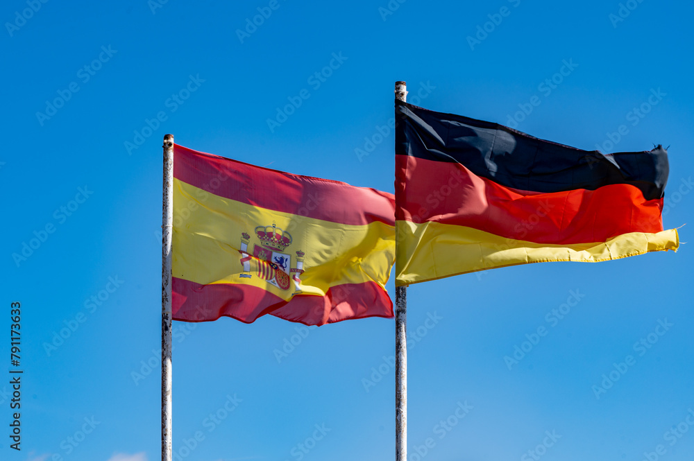 Spanish and German flags on flagstaffs and blue sky Spanish and German flags on flagstaffs and blue sky