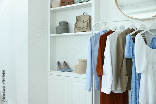 Rack with different clothes near shelving unit with shoes and bags indoors