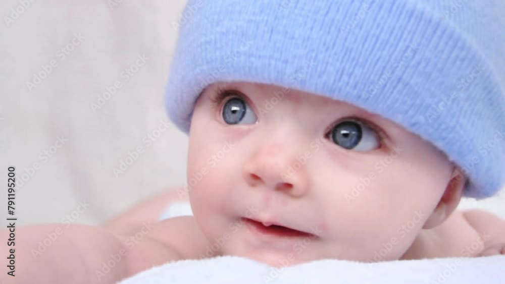 A little boy baby is hiding under a blue blanket with a hat on. He is staring at the camera and posing on his tummy. A little boy baby is hiding under a blue blanket with a hat on. He is staring at the camera and posing on his tummy.